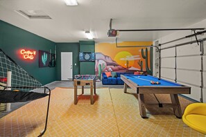 Una habitación con mesa de fútbol, mesa de billar y un mural en la pared.