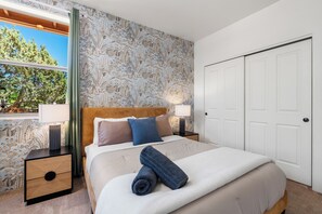 Une chambre d’hôtel comprenant un lit, une table de chevet, une lampe, une armoire et une fenêtre donnant sur des arbres.
