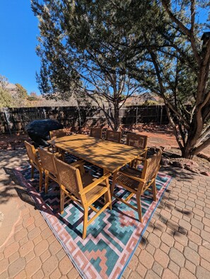 A wooden table with six chairs, a patterned rug, and a tree in the background.