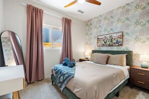 Un dormitorio con cama, mesita de noche, lámpara, espejo y ventana con cortinas.