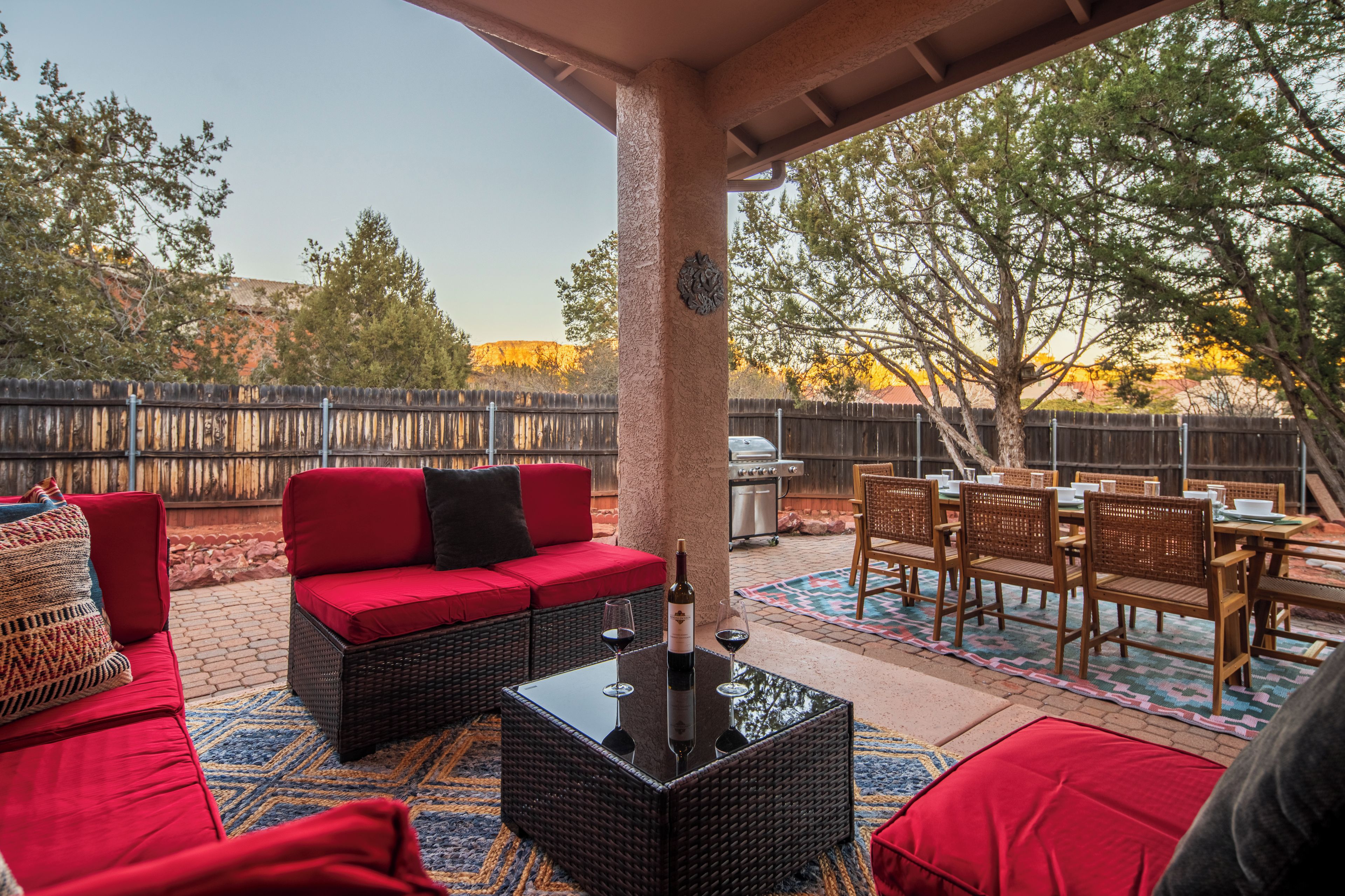 Une terrasse extérieure avec un canapé rouge, des meubles en osier et une table à manger dressée pour un repas.