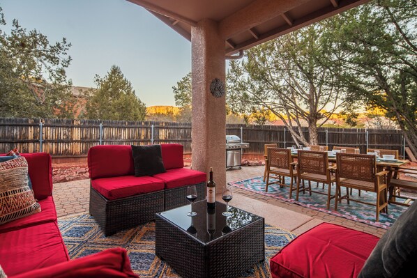 An outdoor patio with a red sofa, wicker furniture, and a dining table set for a meal.
