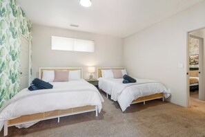 Habitación de hotel con dos camas individuales, una mesita de noche pequeña con lámpara y una ventana con persianas.
