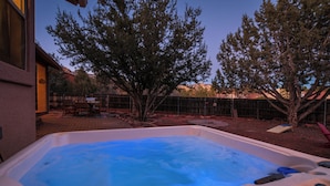 An outdoor hot tub with a digital thermometer, surrounded by trees and a patio area.