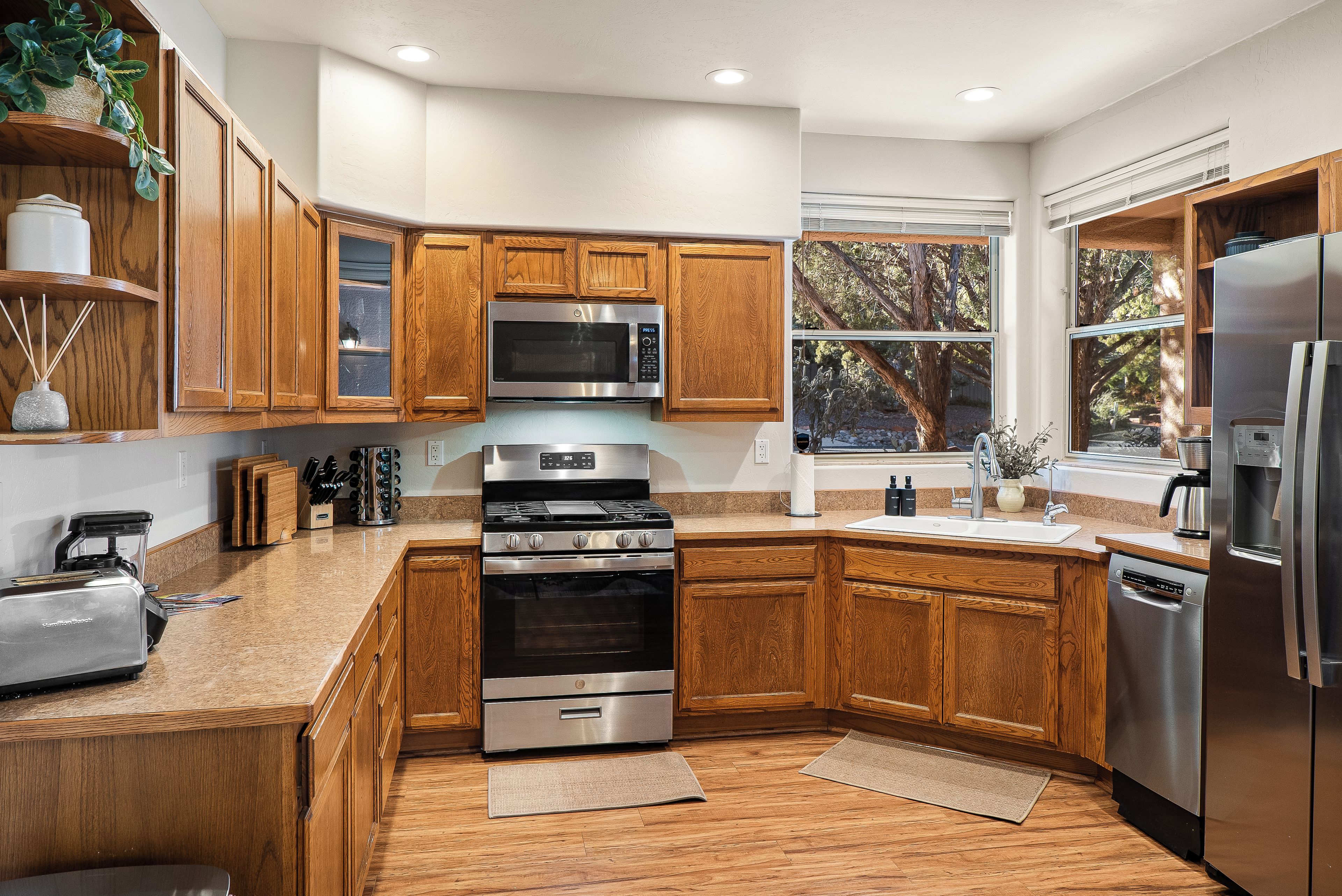 A modern kitchen with wooden cabinets, stainless steel appliances, and a large window.