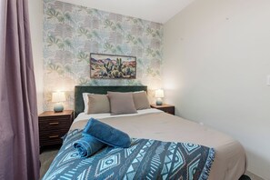 Una habitación de hotel con una cama, dos lámparas de noche, un cuadro de un paisaje desértico y una colcha estampada.