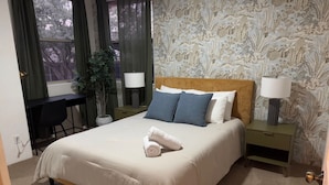 A bedroom with a bed, two bedside tables with lamps, a desk, and a chair.