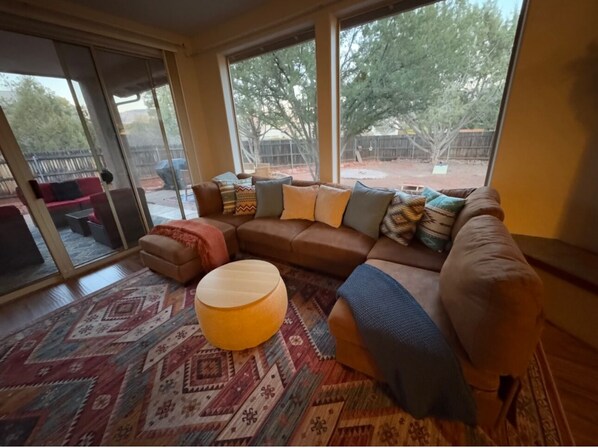 A living room with a brown sofa, patterned rug, and a round wooden ottoman.