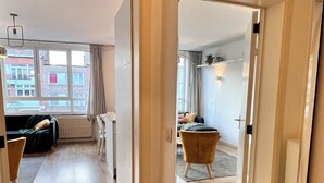 A spacious hallway with a wooden floor leading to a living area with a sofa and a chair. - Bright & Stylish in Nature (Brussels)