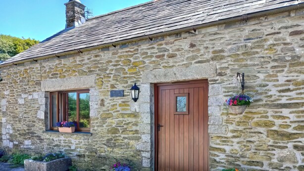 Une maison en pierre avec une porte en bois, une fenêtre agrémentée d’une jardinière et un petit porche.