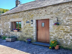 A stone house with a wooden door, a window with a flower box, and a small porch area.