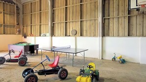 Un grand espace intérieur comprenant une table de ping-pong, une petite table et divers jouets pour enfants.