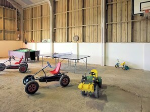 Un grand espace intérieur comprenant une table de ping-pong, une petite table et divers jouets pour enfants.