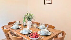 Une table à manger dressée avec des assiettes, des bols, des couverts et un saladier rempli de fraises.