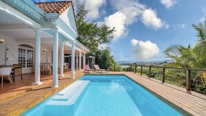 Une piscine avec une terrasse en bois, des colonnes blanches et une vue sur la mer.