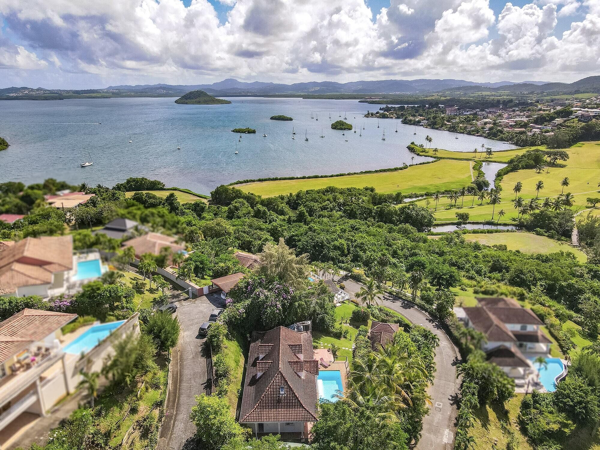 Un resort costero con varias piscinas, abundante vegetación y vistas al mar con barcos.