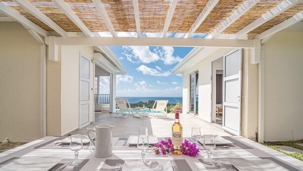 A dining table set for two with a view of the ocean and a pool in the background. - Domaine Agapé - Four Bedroom Villa, Sleeps 9 (Le Diamant)