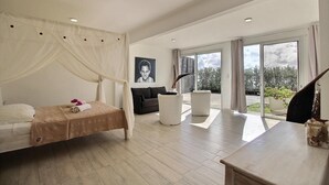 A modern bedroom with a canopy bed, a sofa, a dining table, and a large sliding glass door leading to a balcony. - Domaine Agapé - Four Bedroom Villa, Sleeps 9 (Le Diamant)