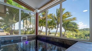 An indoor swimming pool with a view of palm trees and a clear sky.