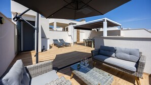 Una terrassa al terrat amb un parasol gran, mobles de vusta i una zona de menjador.