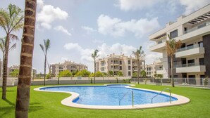 Una piscina envoltada de gespa verda i palmeres, amb edificis moderns al fons.