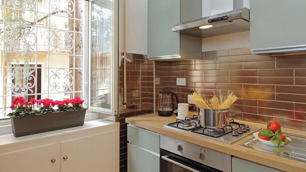 A kitchen with a gas stove, a pot, a kettle, and a window with decorative iron bars. - TM APARTMENT (Roma)