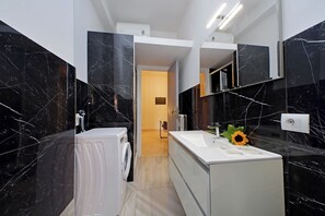 A modern bathroom with black marble walls, a white sink, and a washing machine. - TM APARTMENT (Roma)