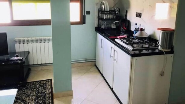 Une cuisine de taille réduite, équipée d’une cuisinière à gaz, d’un évier et d’une fenêtre située au-dessus du plan de travail.