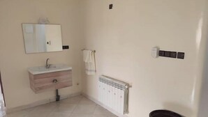 A bathroom with a wooden vanity, a mirror, a towel rack, a radiator, and a trash can. - Escale. 1!!

 (Midelt)
