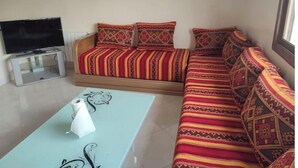 A living room with a sofa, a TV on a stand, and a glass coffee table. - Escale. 1!!

 (Midelt)