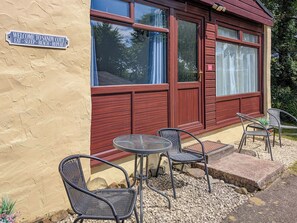 A building with a sign reading 'WELCOME TO SANDY COTT,' outdoor seating with chairs and a table, and a window with curtains. - 2 bedroom accommodation in Kilkhampton (Kilkhampton)