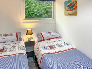 Un dormitorio con dos camas, una mesita de noche con lámpara, una ventana con vistas a la vegetación y un cuadro en la pared.
