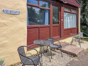 A building with a sign reading 'WELCOME TO SANDY COTT,' outdoor seating with chairs and a table, and a window with curtains.