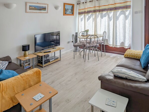 A living room with a TV, sofa, chairs, a small table, and a dining area.