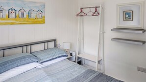 Makuuhuoneessa on sänky, yöpöytä lampun kanssa, seinälle ripustettu vaateteline ja taulu seinällä.