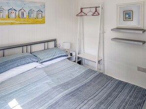 A bedroom with a bed, a bedside table with a lamp, a hanging clothes rack, and a painting on the wall. - 2 bedroom accommodation in Kilkhampton (Kilkhampton)