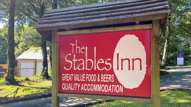 The Stables Inn -majatalon kyltti, jossa korostetaan sen edullisia ruoka- ja juomatarjoiluja sekä laadukasta majoitusta.
