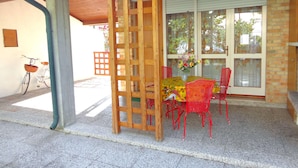 Un patio techado con una mesa de madera y sillas rojas, una bicicleta y una escalera de madera.