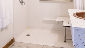 Une salle de bain moderne avec une douche à l’italienne, des barres d’appui, un lavabo blanc avec un récipient en bois et un rideau de douche blanc.