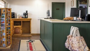 Un comptoir d’accueil avec un ordinateur, une machine à café et un meuble en bois contenant des cartes postales.