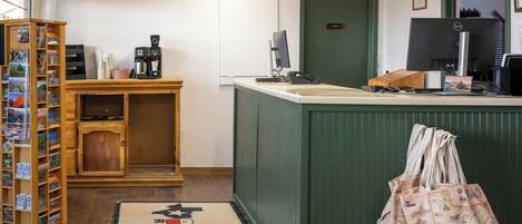 Een receptiebalie met een computer, een koffieapparaat en een houten kastje met ansichtkaarten.
