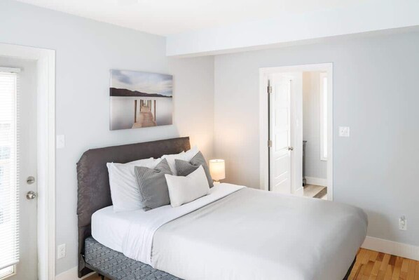 A bedroom with a bed, a nightstand, a lamp, and a painting on the wall. - 86A King Bed 2bd 3bt on Queen St. Downtown (Charlottetown)