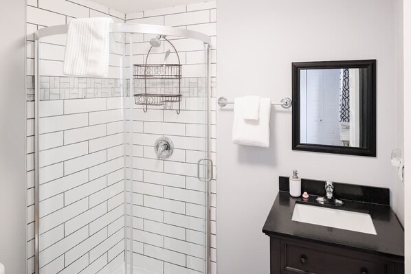 Un baño con cabina de ducha de vidrio, lavamanos con encimera negra y espejo superior.