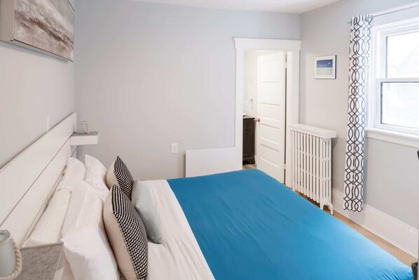 A bedroom with a bed, a dresser, a radiator, and a window with a curtain. - 86A King Bed 2bd 3bt on Queen St. Downtown (Charlottetown)