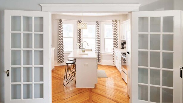 Una cocina con una isla central, piso de madera y armarios blancos.