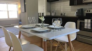 Una cocina moderna con armarios blancos, un horno de acero inoxidable y una zona de comedor con sillas blancas y una mesa blanca.