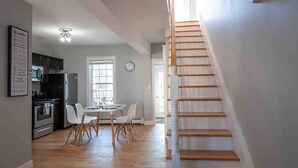 Una cocina moderna con armarios blancos, un comedor con mesa y sillas, y una escalera de madera.