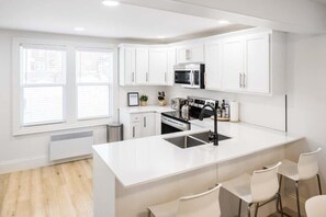 Una cocina moderna con armarios blancos, una isla central con taburetes de bar, un microondas y un tostador.