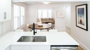 Una cuina moderna amb una illa central, armaris blancs i una zona de menjador amb taula rodona i cadires.