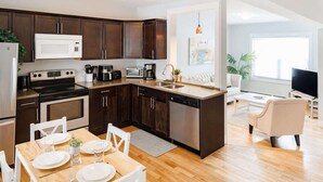 A modern kitchen with dark cabinets, a white microwave, a stove, and a dishwasher. There is a dining area with a wooden table and chairs. - 67 - Walking distance to downtown (Charlottetown)